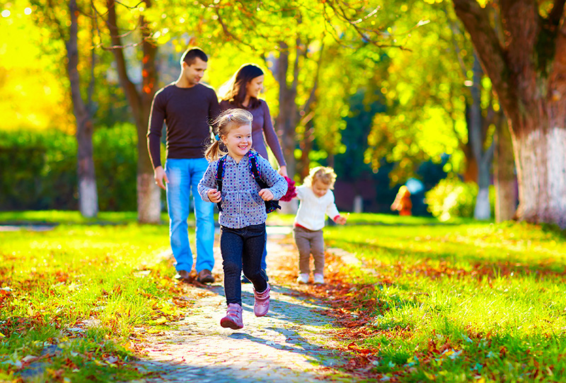 happy young girl running in autumn park with her family on background